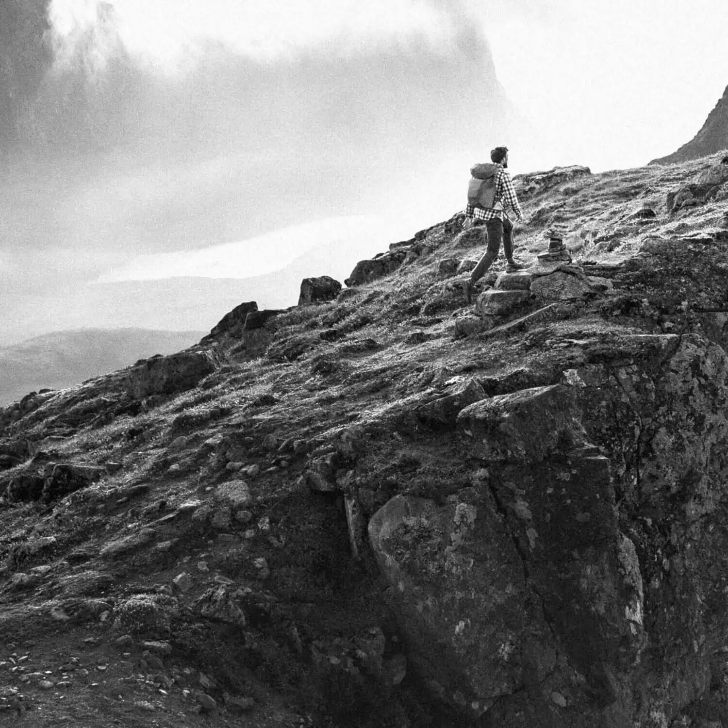 black and white photo of a man climbing a mountain with a backpack